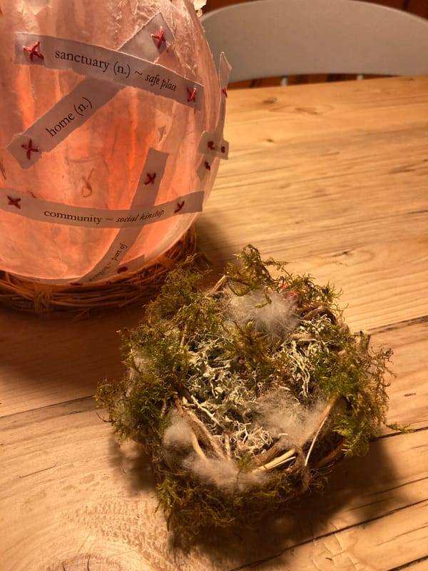 Lisa's artwork a nest made of moss and twigs and a lantern light with values such as Community, Home and Sanctuary on it.